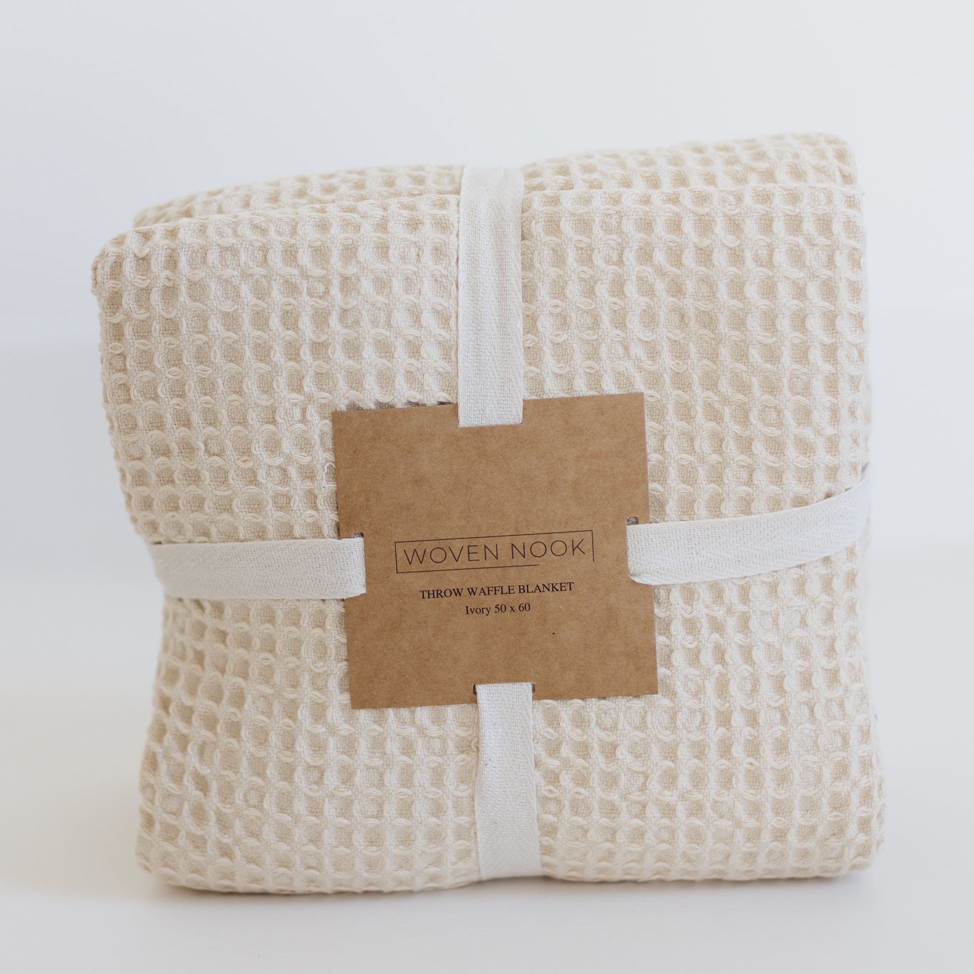 Ivory waffle blanket with textured grid pattern, rolled and wrapped with cream cotton band and kraft paper label.