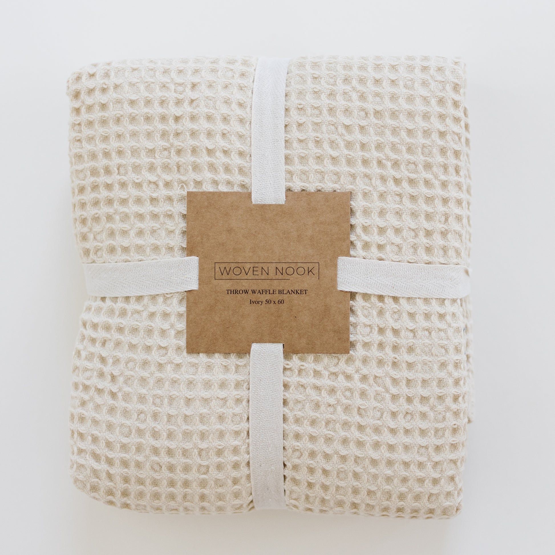 Ivory waffle blanket rolled and tied with white ribbon and kraft paper band label.