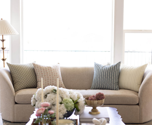 Four decorative pillows in various patterns including geometric, striped, and textured designs in neutral and blue tones arra