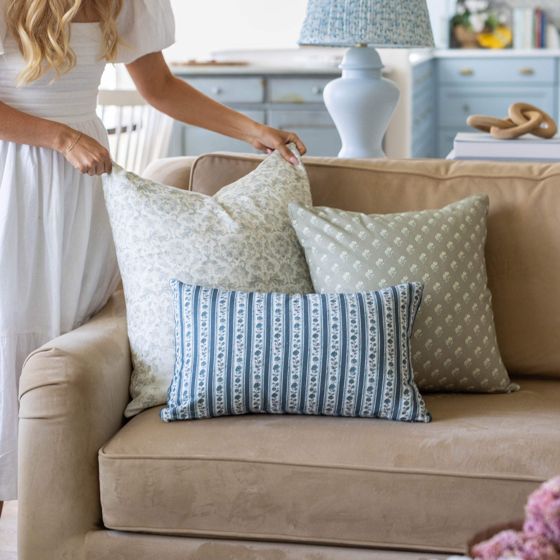 Three decorative pillows in green and blue patterns arranged on a beige sofa.