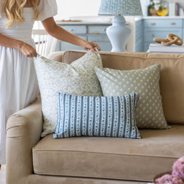 Three decorative pillows in green and blue patterns arranged on a beige sofa.