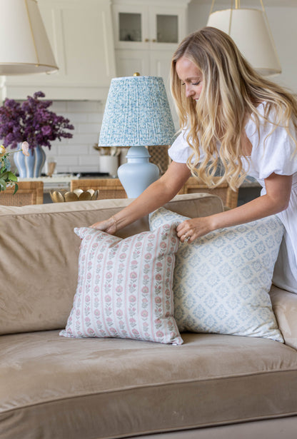 Woman arranging two decorative pillows with floral and geometric patterns on a beige sofa.