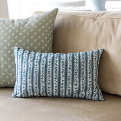 Blue and white striped rectangular pillow with repeating botanical pattern on cream sofa.
