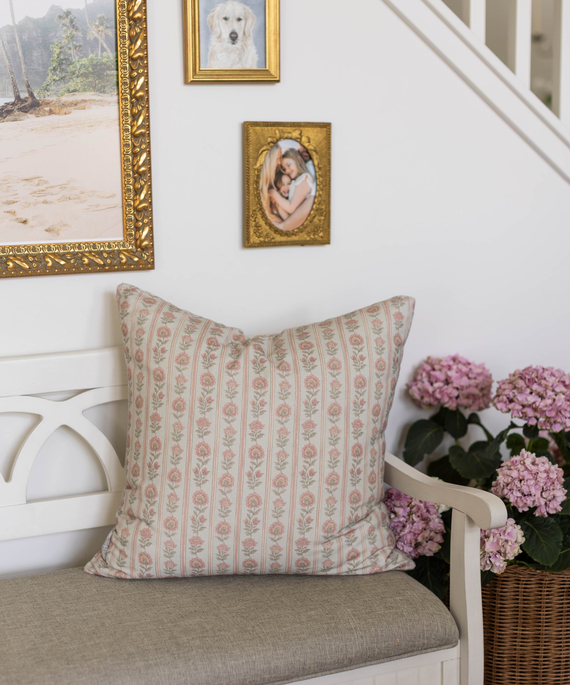 Beige pillow with pink floral stripe pattern displayed on white chair next to pink hydrangeas.