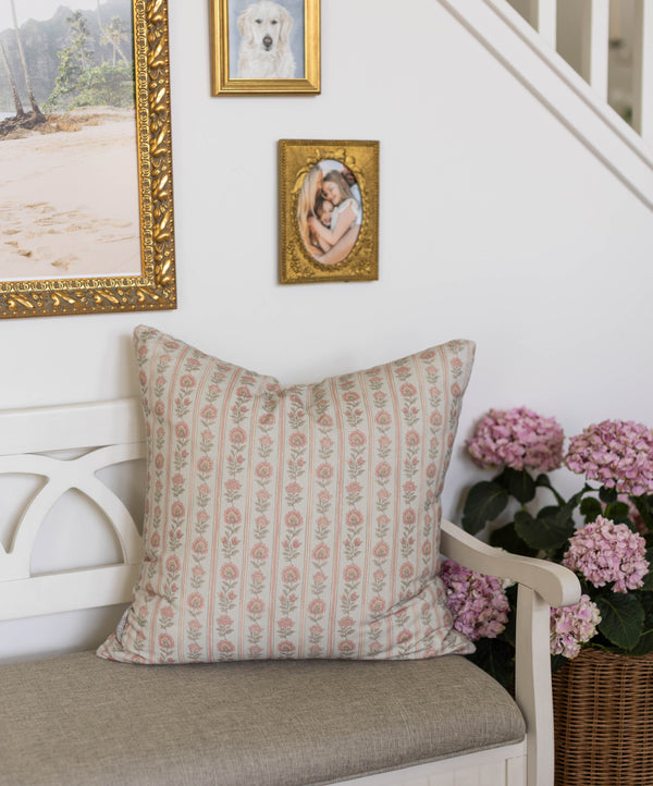 Beige pillow with pink floral stripe pattern displayed on white chair next to pink hydrangeas.
