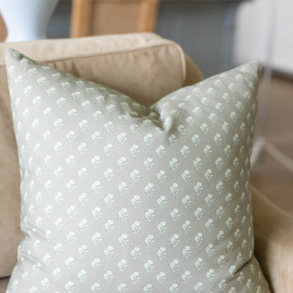 Sage green pillow with white floral pattern, displayed on beige sofa.