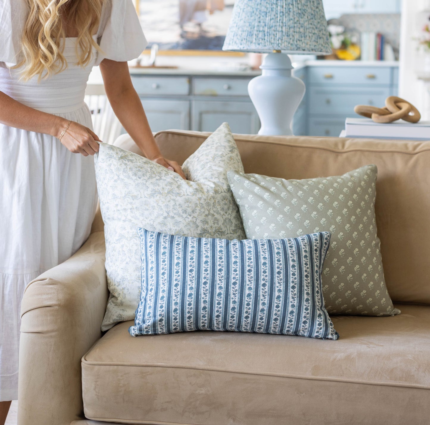 Three decorative pillows in cream, sage, and blue stripe patterns arranged on a beige sofa.