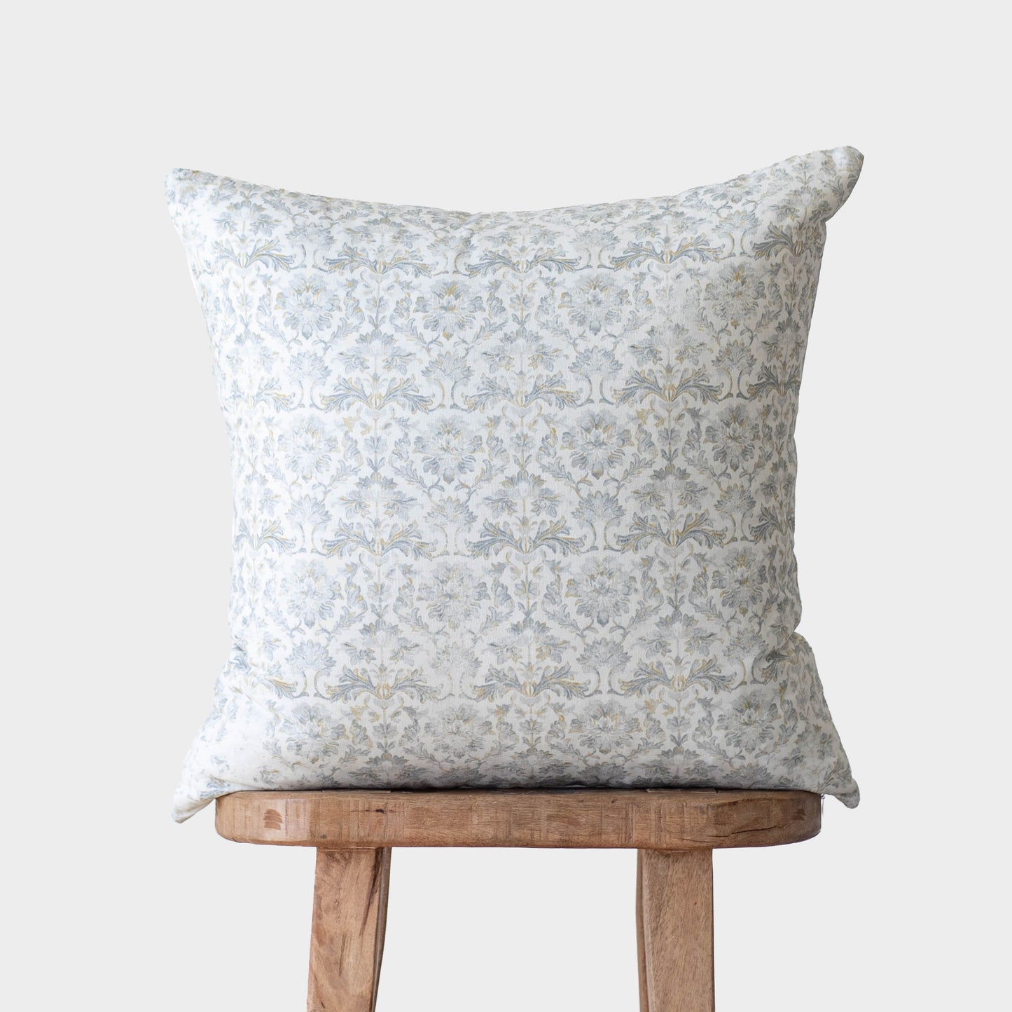 Square throw pillow with gray damask pattern on white fabric, displayed on wooden chair.