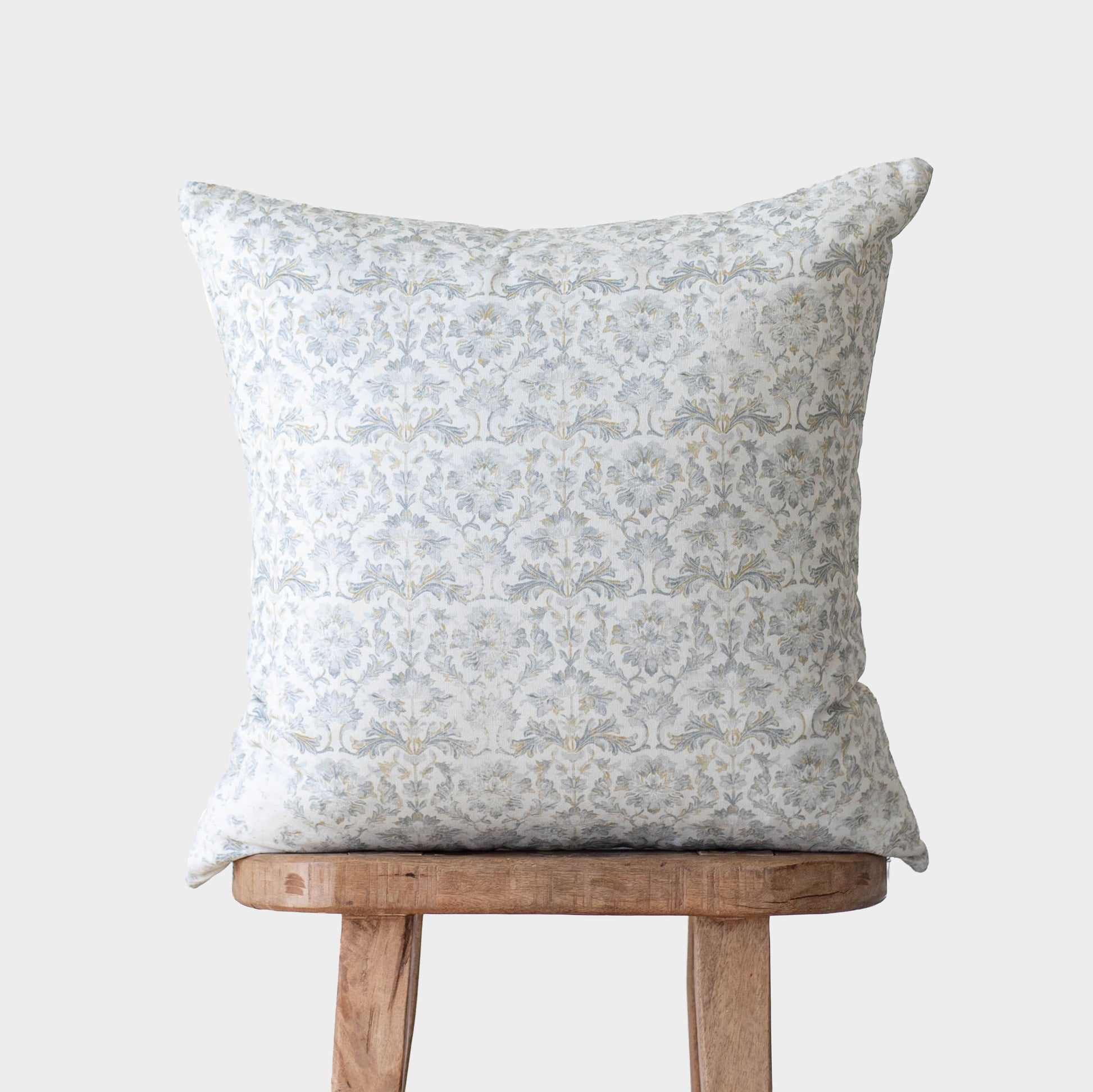 Square throw pillow with gray damask pattern on white fabric, displayed on wooden chair.