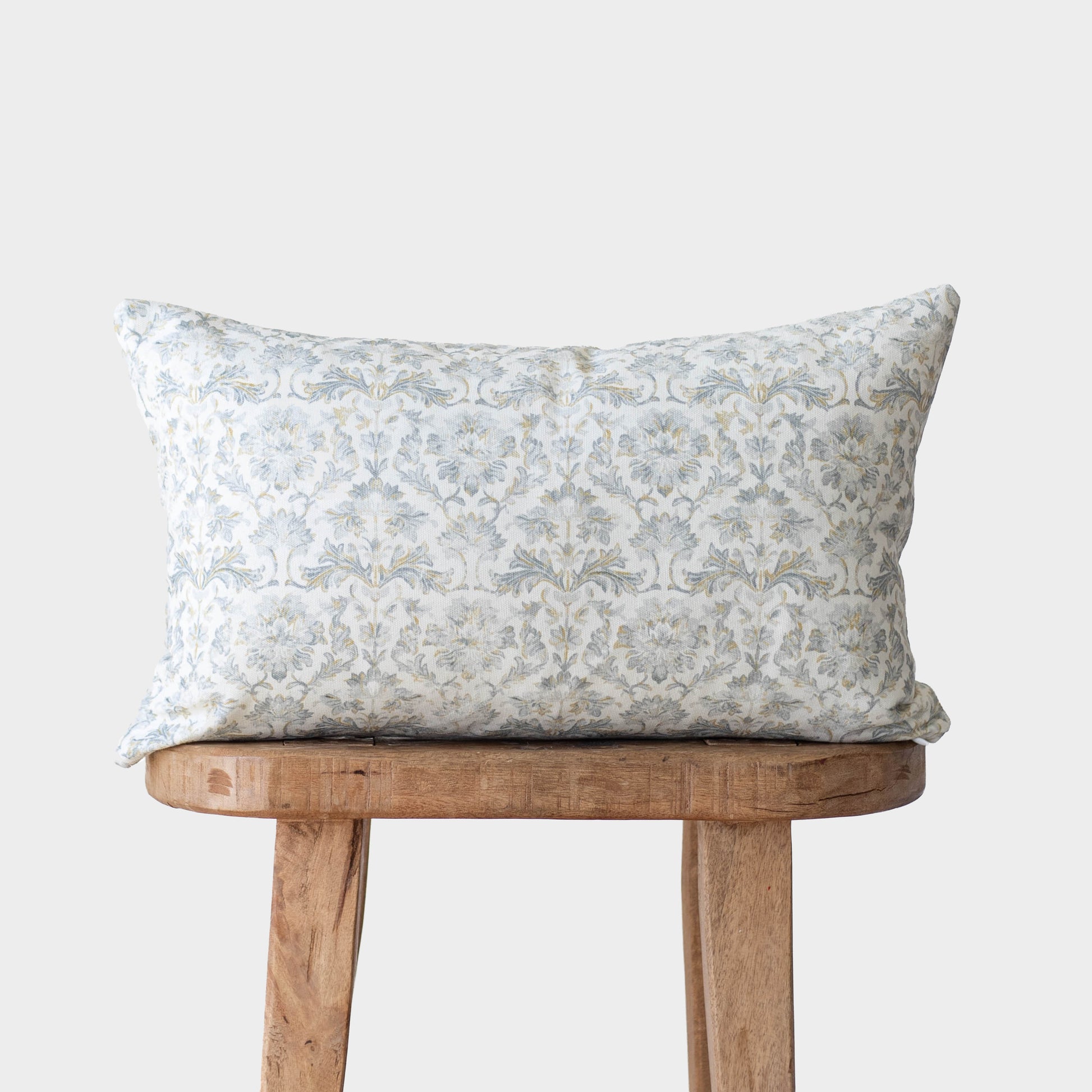 Gray damask patterned pillow on wooden bench against white background.