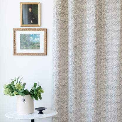 Two cream and taupe damask patterned curtain panels hanging at a window, displayed in a room with framed artwork and potted p