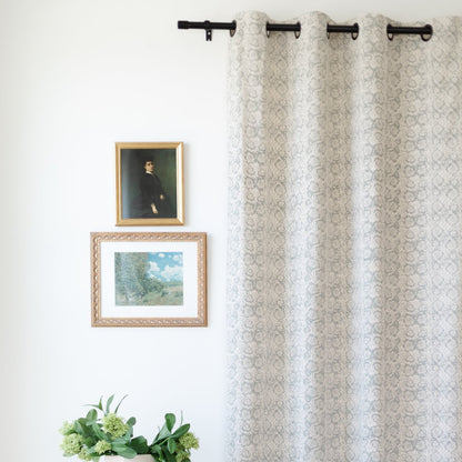 Two beige curtain panels with damask pattern hung on black grommet rod.