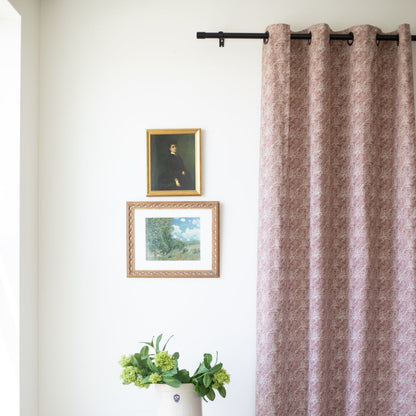 Two mauve textured curtain panels with grommet top hanging from black rod on white wall.