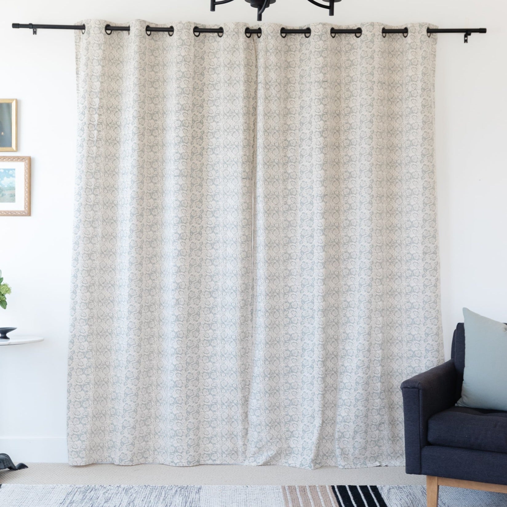 Two beige patterned curtain panels with grommet tops hanging on a black rod.