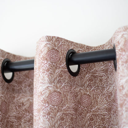 Pair of mauve curtain panels with botanical print pattern hung on black rod with grommet top rings.