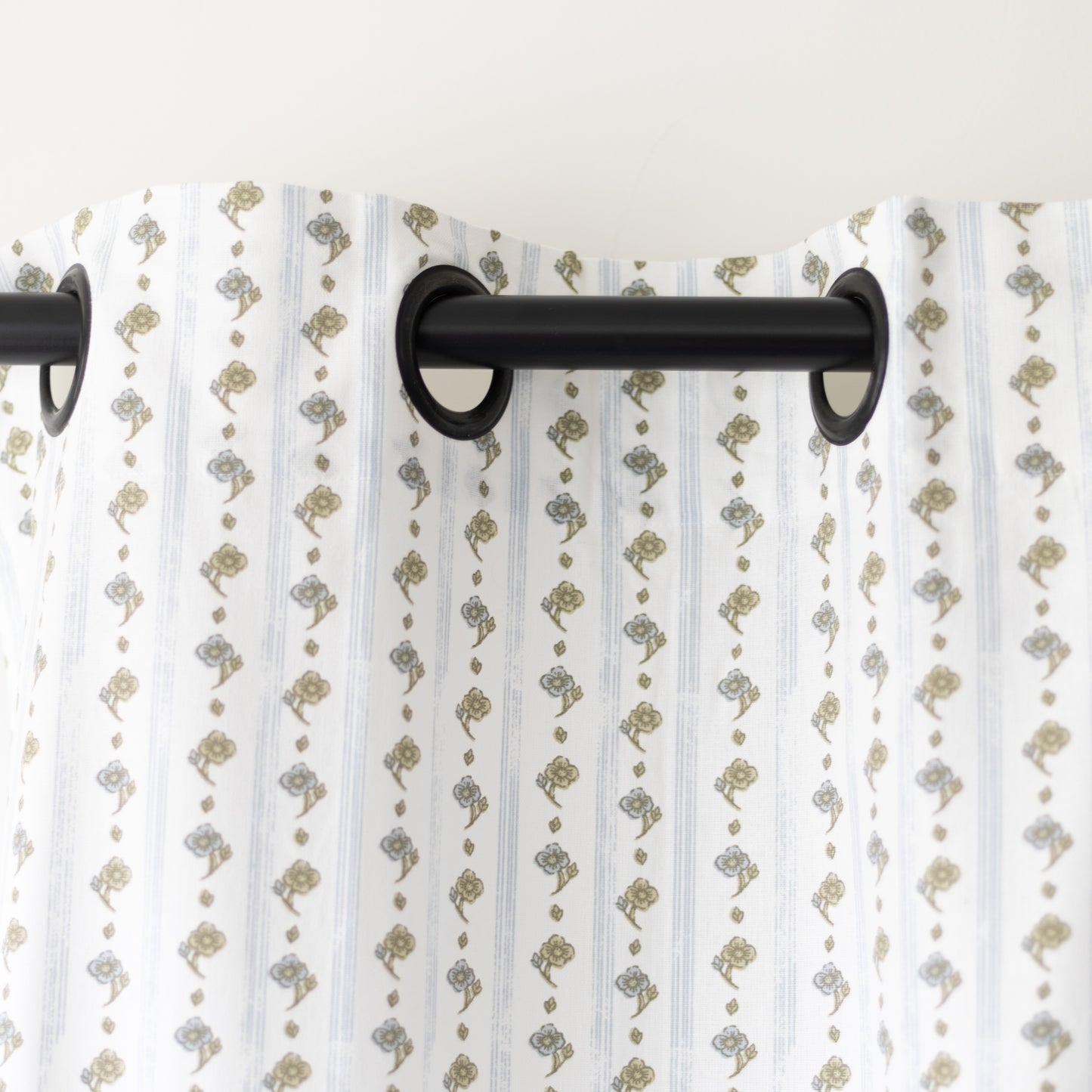 Two white curtain panels with tan and gray botanical print pattern hung on black rod.