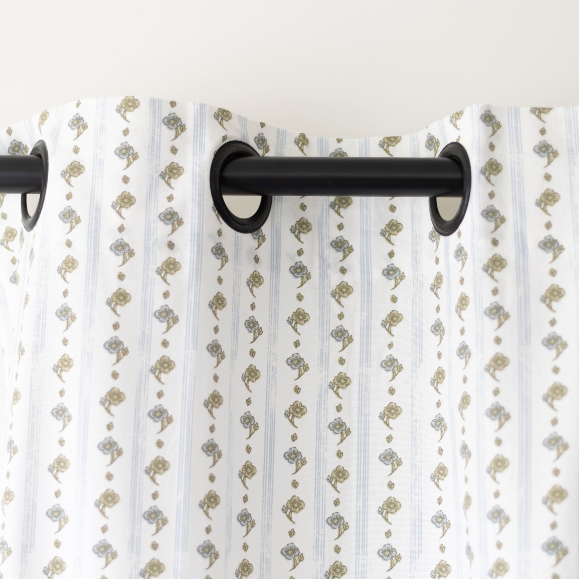 Two white curtain panels with tan and gray botanical print pattern hung on black rod.