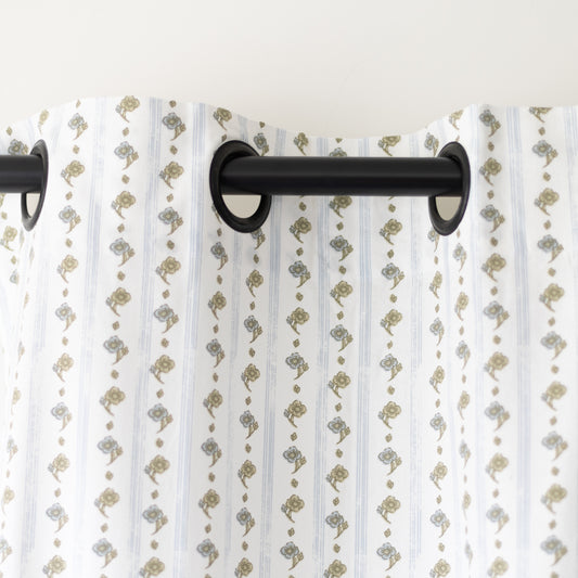 Two white curtain panels with tan and gray botanical print pattern hung on black rod.