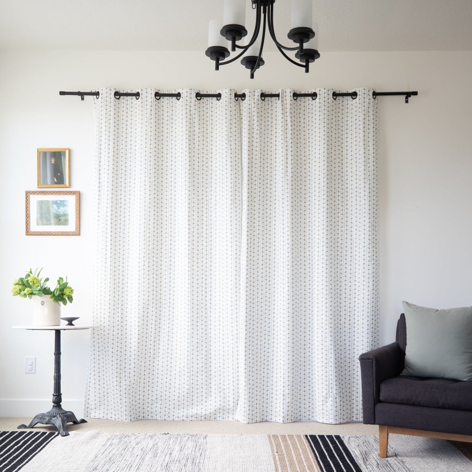 Two white curtain panels with textured weave pattern hanging from black rod with grommet top.