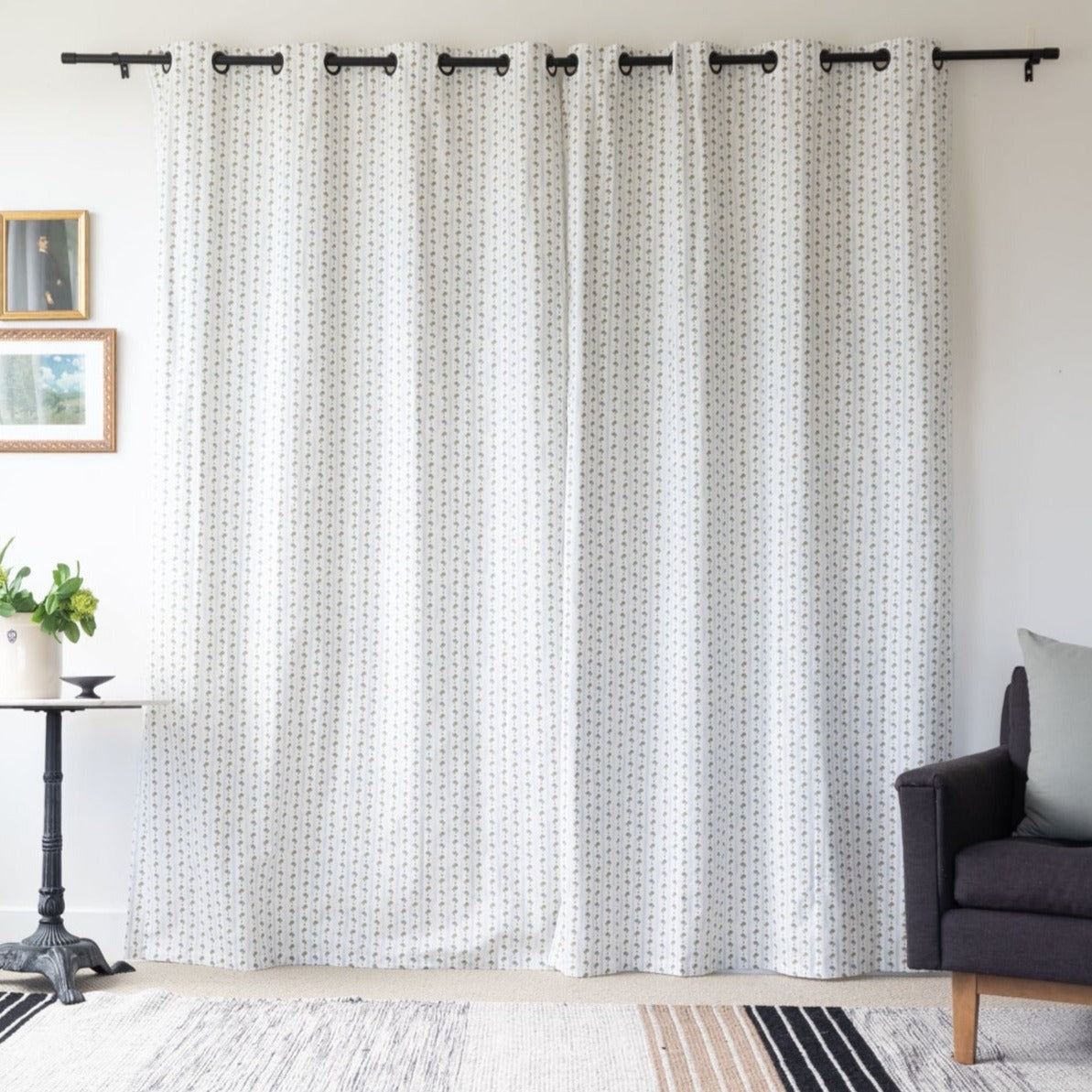 Two cream curtain panels with small geometric pattern and black grommet top rings hanging on black rod.
