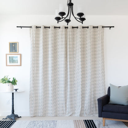 Two beige curtain panels with geometric pattern hanging from black rod with grommet top.