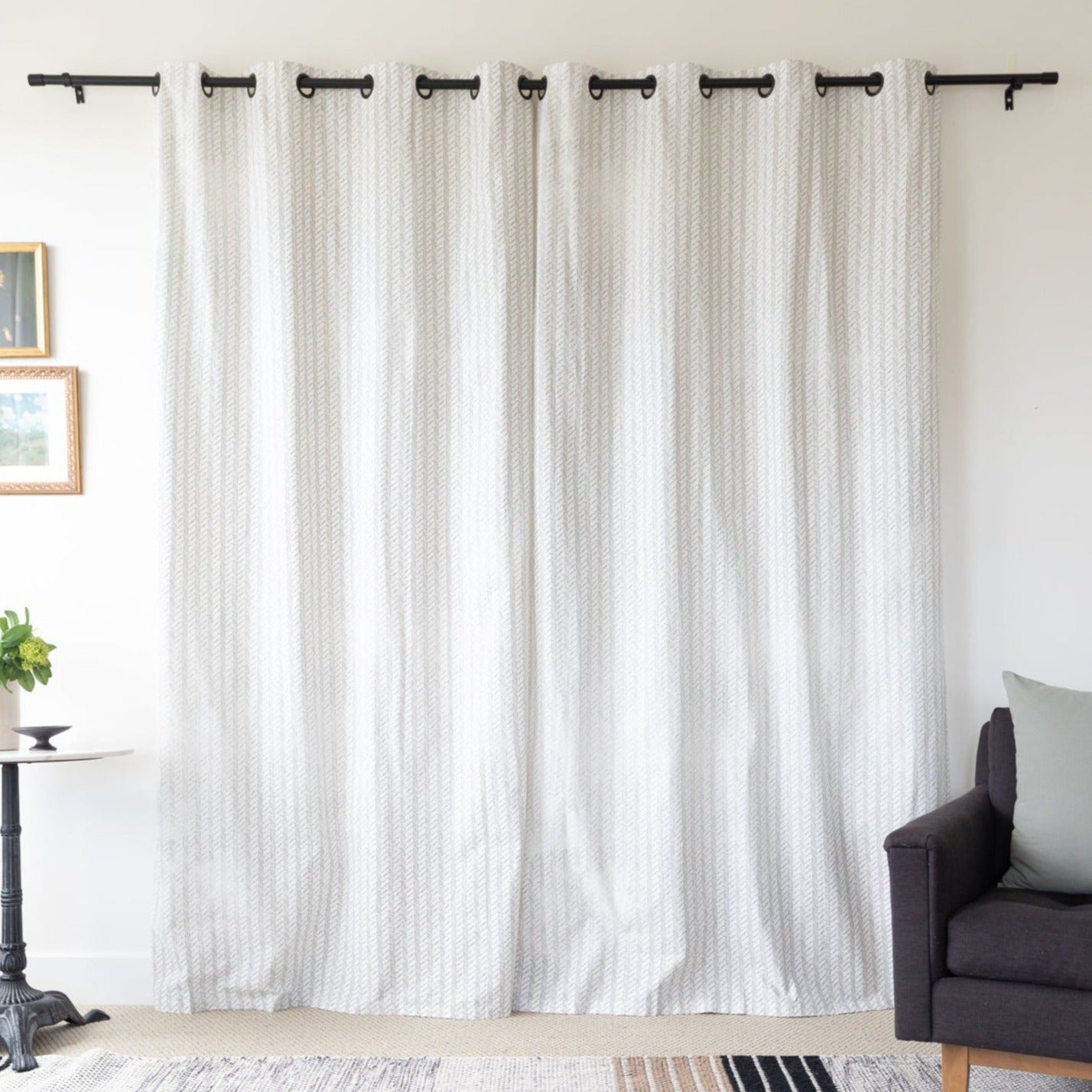 Two cream textured curtain panels with grommet tops hanging on a black rod in a living room setting.