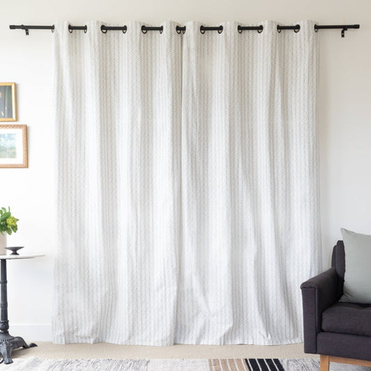 Two cream textured curtain panels with grommet tops hanging on a black rod in a living room setting.