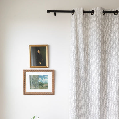 Two light gray curtain panels with textured weave pattern hanging from black rod with grommet rings.