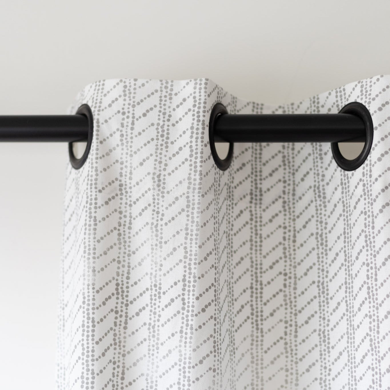 Two white curtain panels with gray diagonal dot pattern hanging from black grommet rings on a rod.