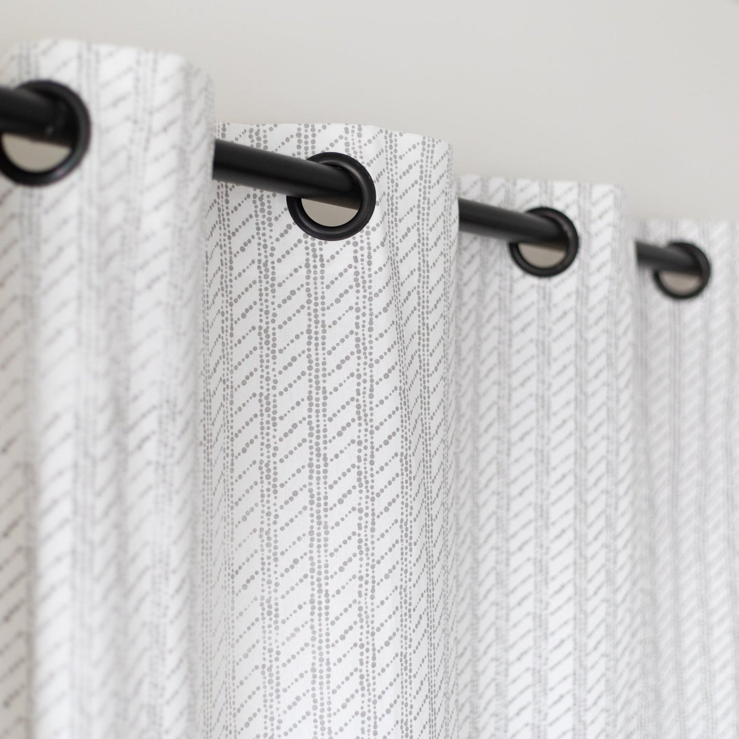 Two white curtain panels with diagonal textured pattern and black grommet top rings on a rod.