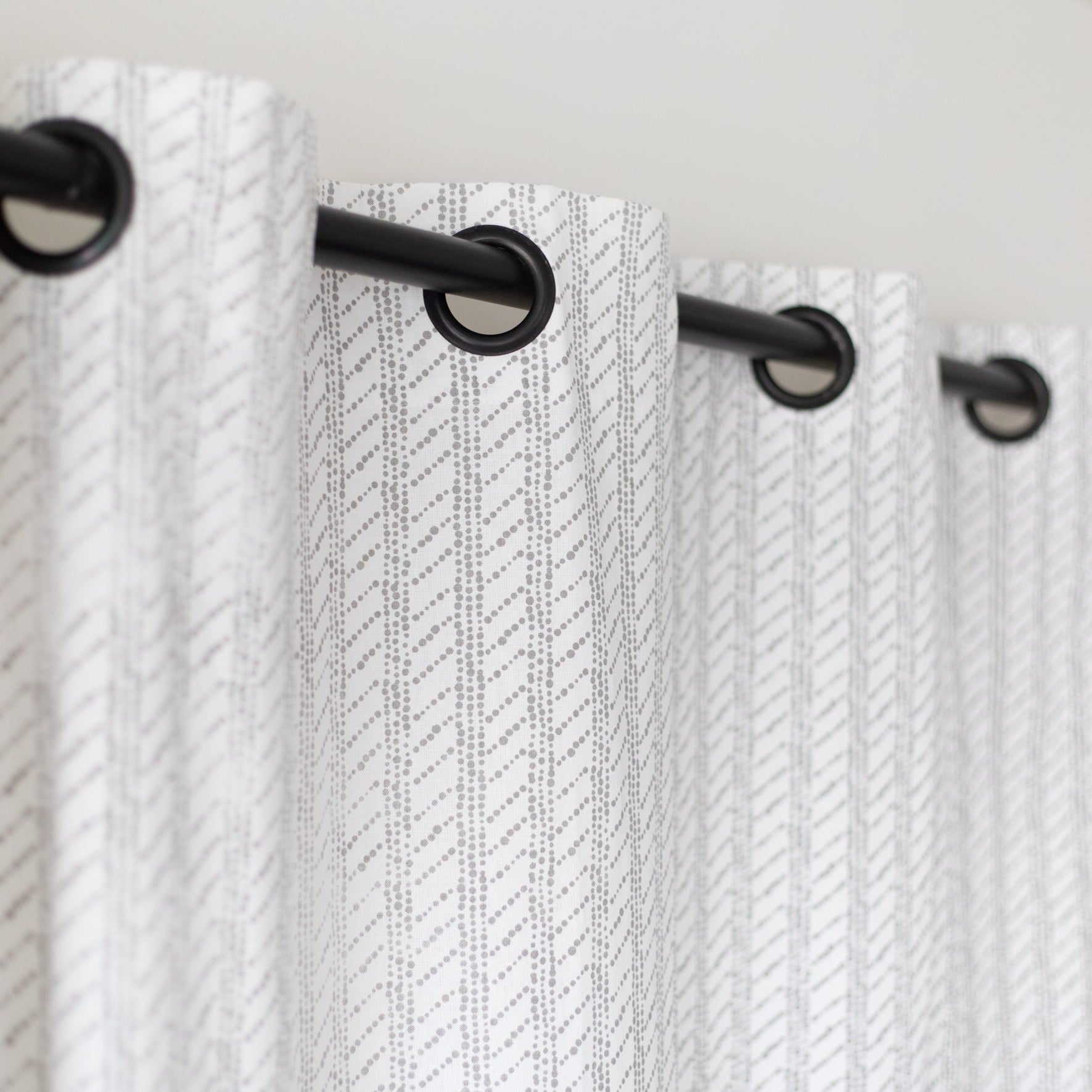 Two white curtain panels with diagonal textured pattern and black grommet top rings on a rod.