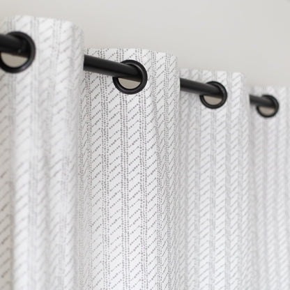 Two white curtain panels with diagonal textured pattern and black grommet top rings on a rod.
