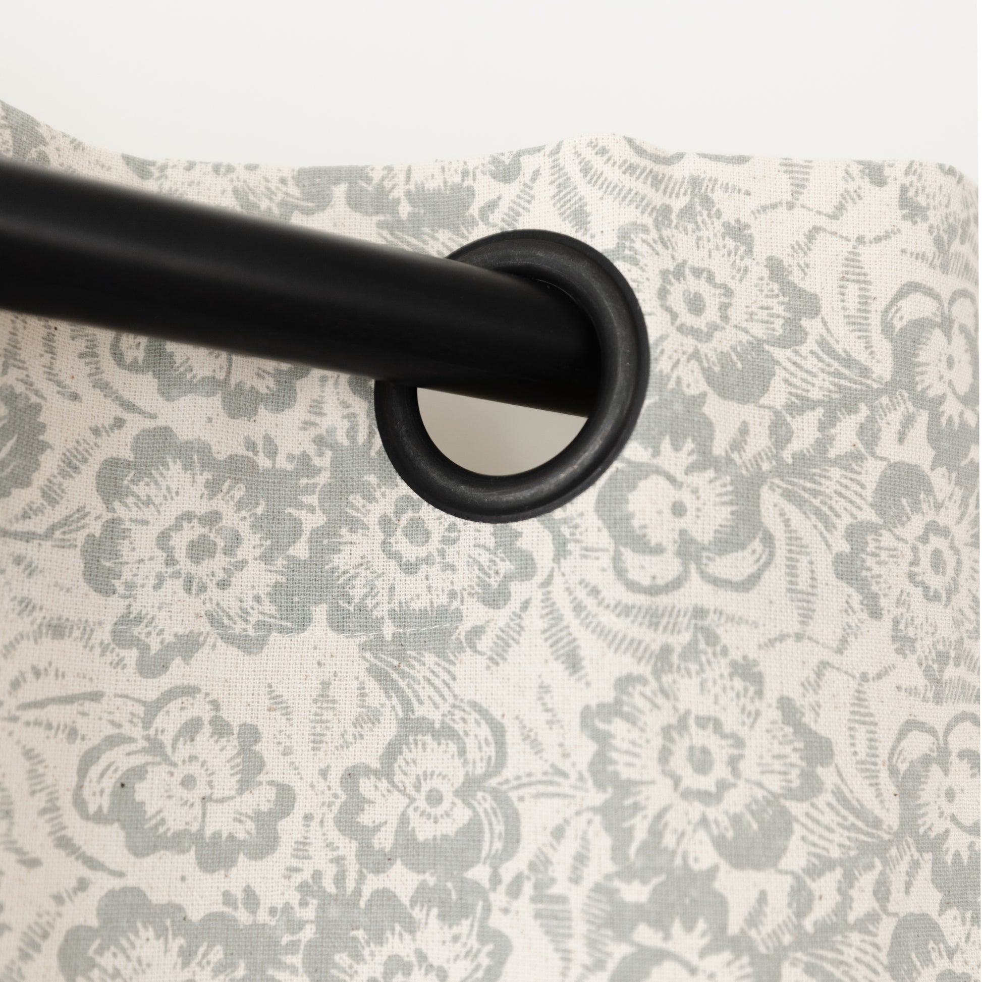 Two cream curtain panels with gray floral pattern hung on black rod with grommet rings.
