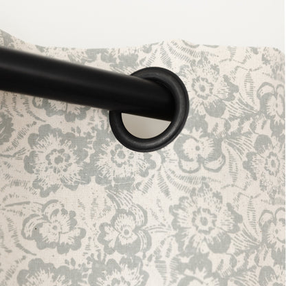 Two cream curtain panels with gray floral pattern hung on black rod with grommet rings.