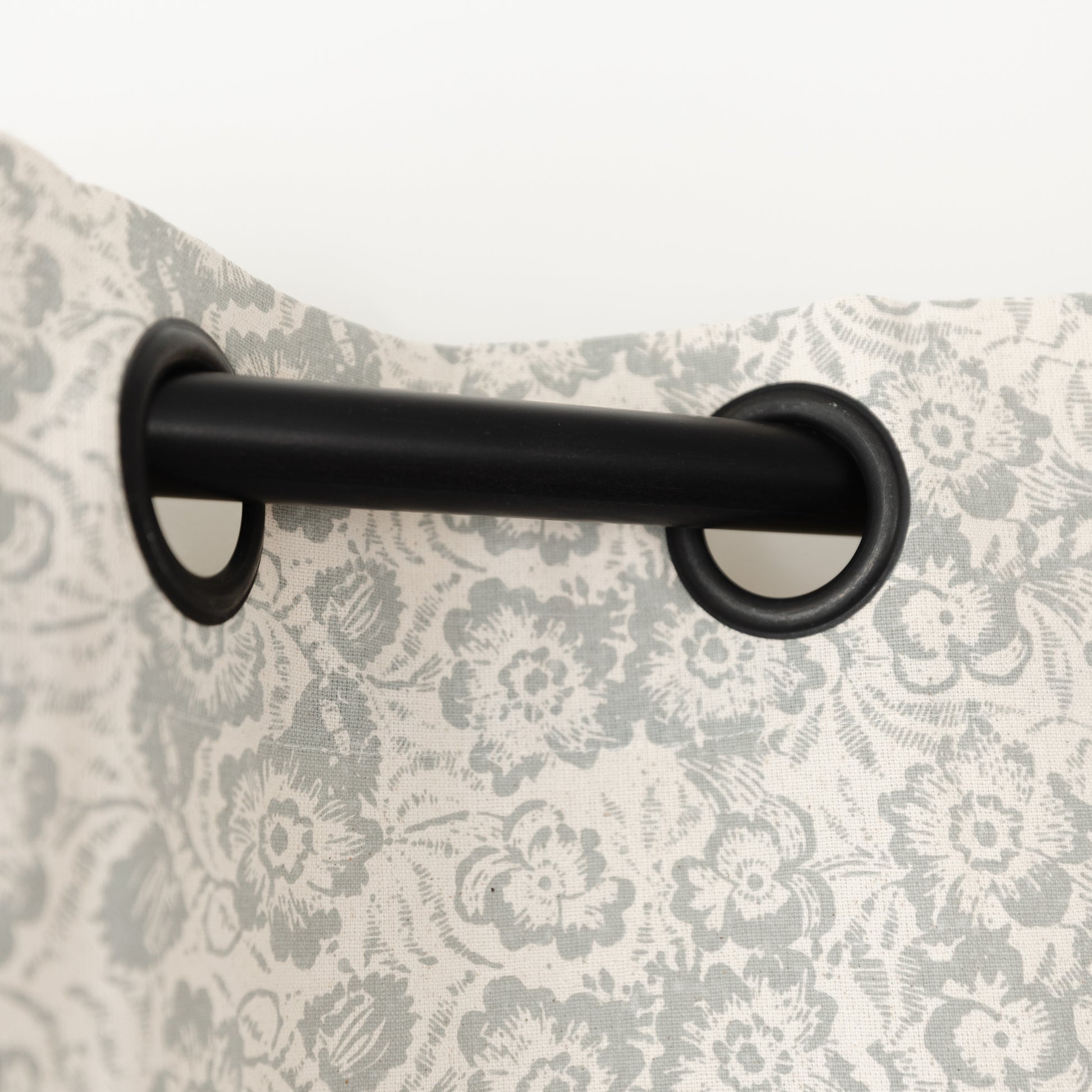 Two cream curtain panels with gray floral pattern hung on black grommet rod.