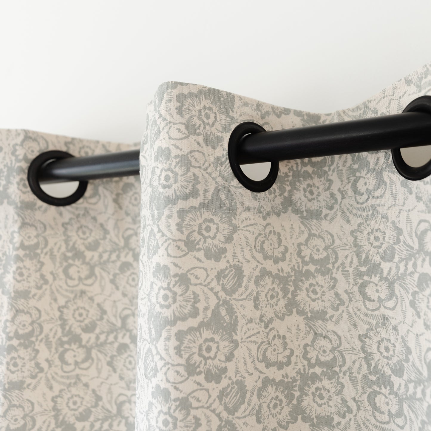Two cream curtains with gray damask floral pattern hanging from black grommet rod.