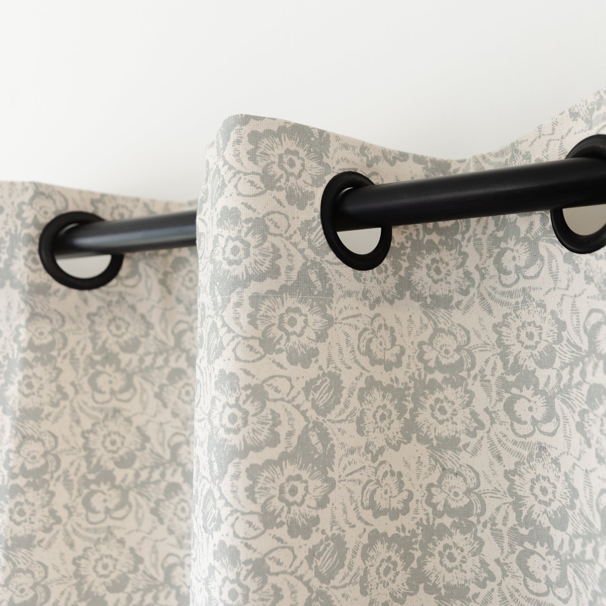 Two cream curtains with gray damask floral pattern hanging from black grommet rod.