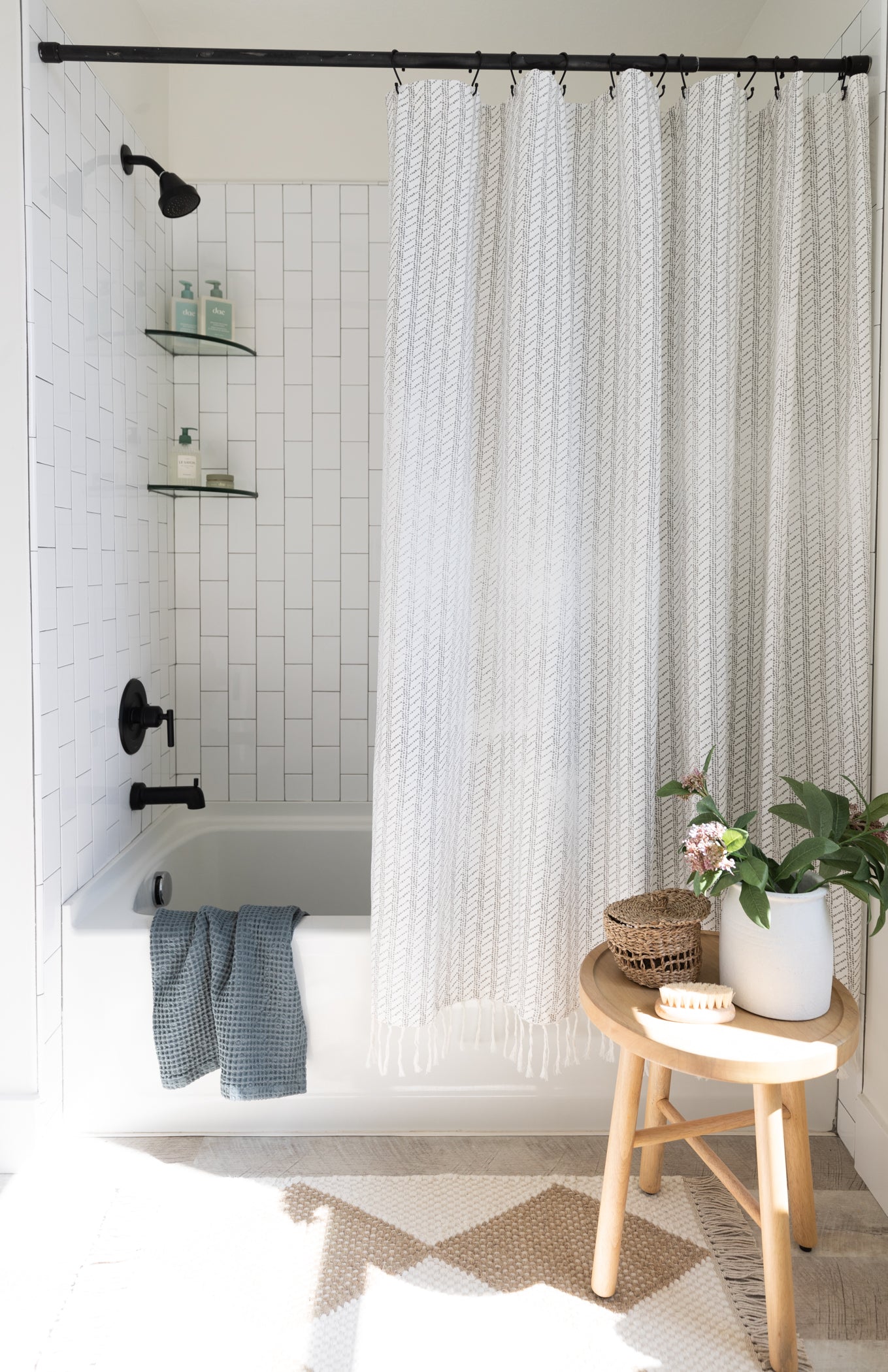 Cream and white woven textured shower curtain with vertical stripe pattern hung on black rod above bathtub.