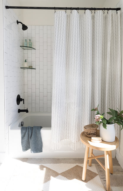 Cream and white woven textured shower curtain with vertical stripe pattern hung on black rod above bathtub.
