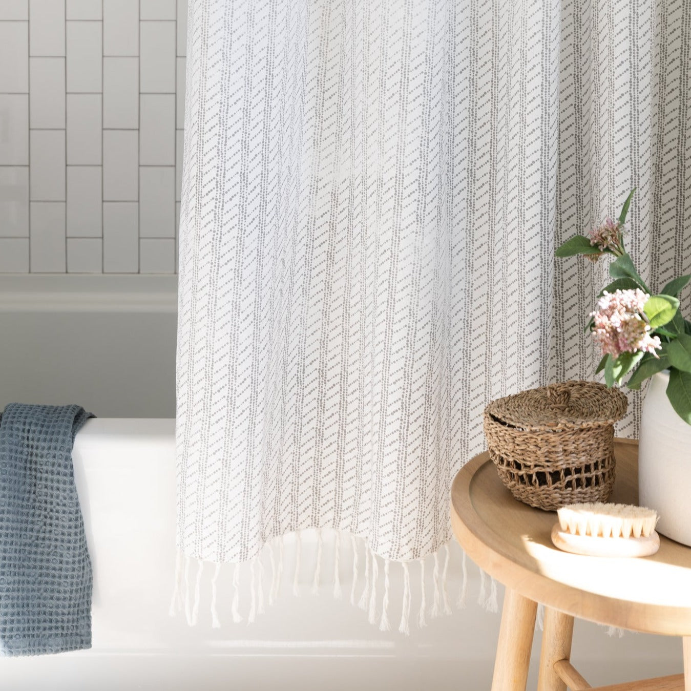 Cream textured shower curtain with vertical chevron pattern and fringe trim hanging in bathroom above white bathtub.
