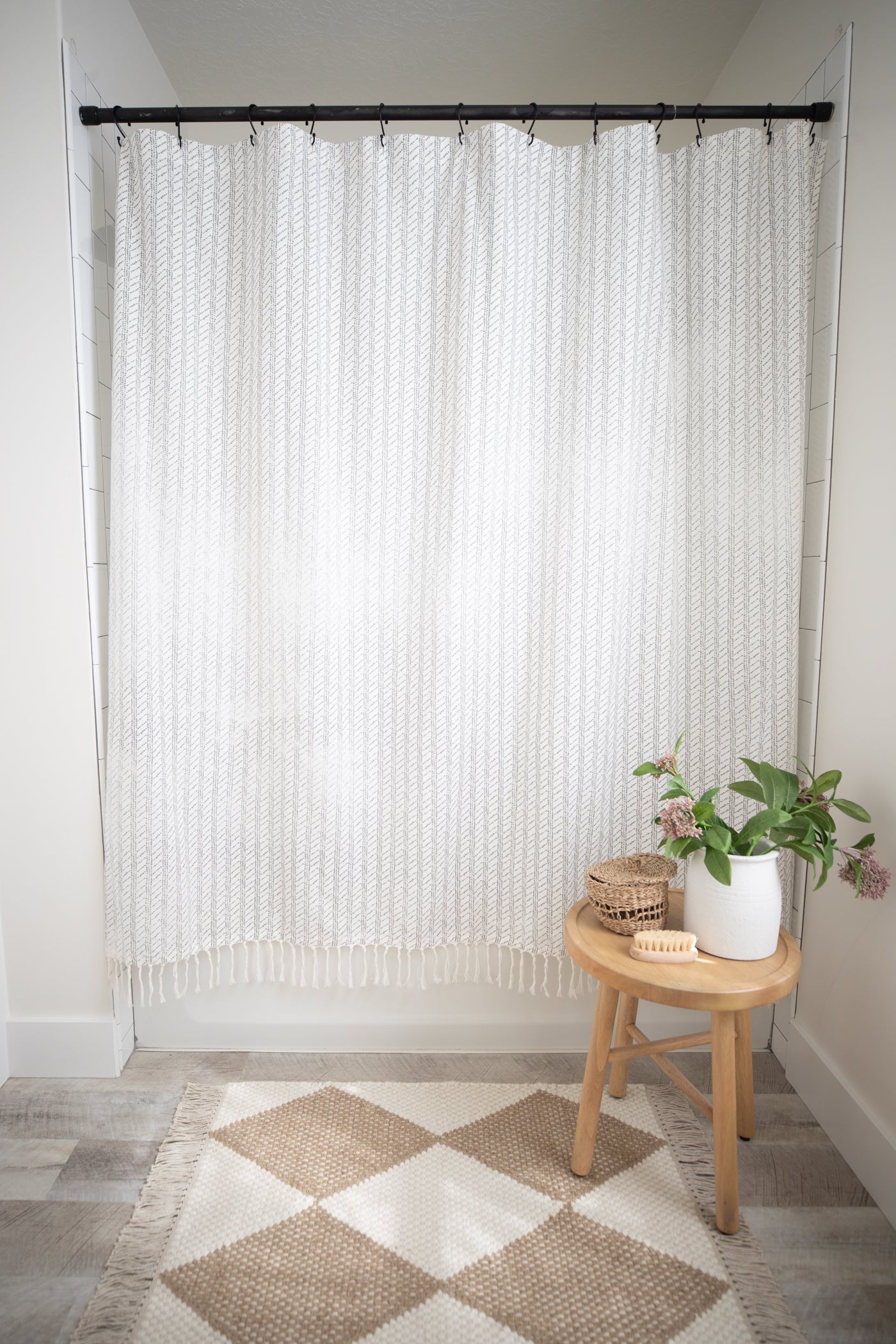 White textured shower curtain with vertical ribbed pattern hanging from black rod with rings in tiled bathroom.