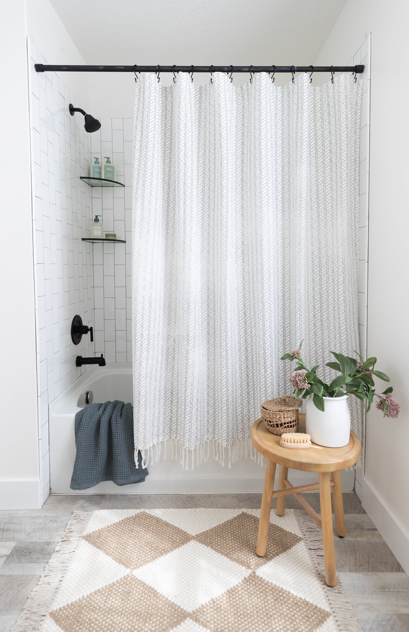White and gray striped shower curtain with textured weave fabric and fringe trim hanging from black rod.