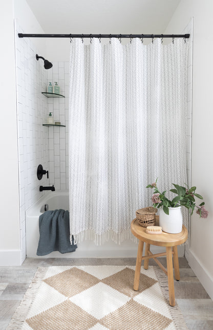 White and gray striped shower curtain with textured weave fabric and fringe trim hanging from black rod.