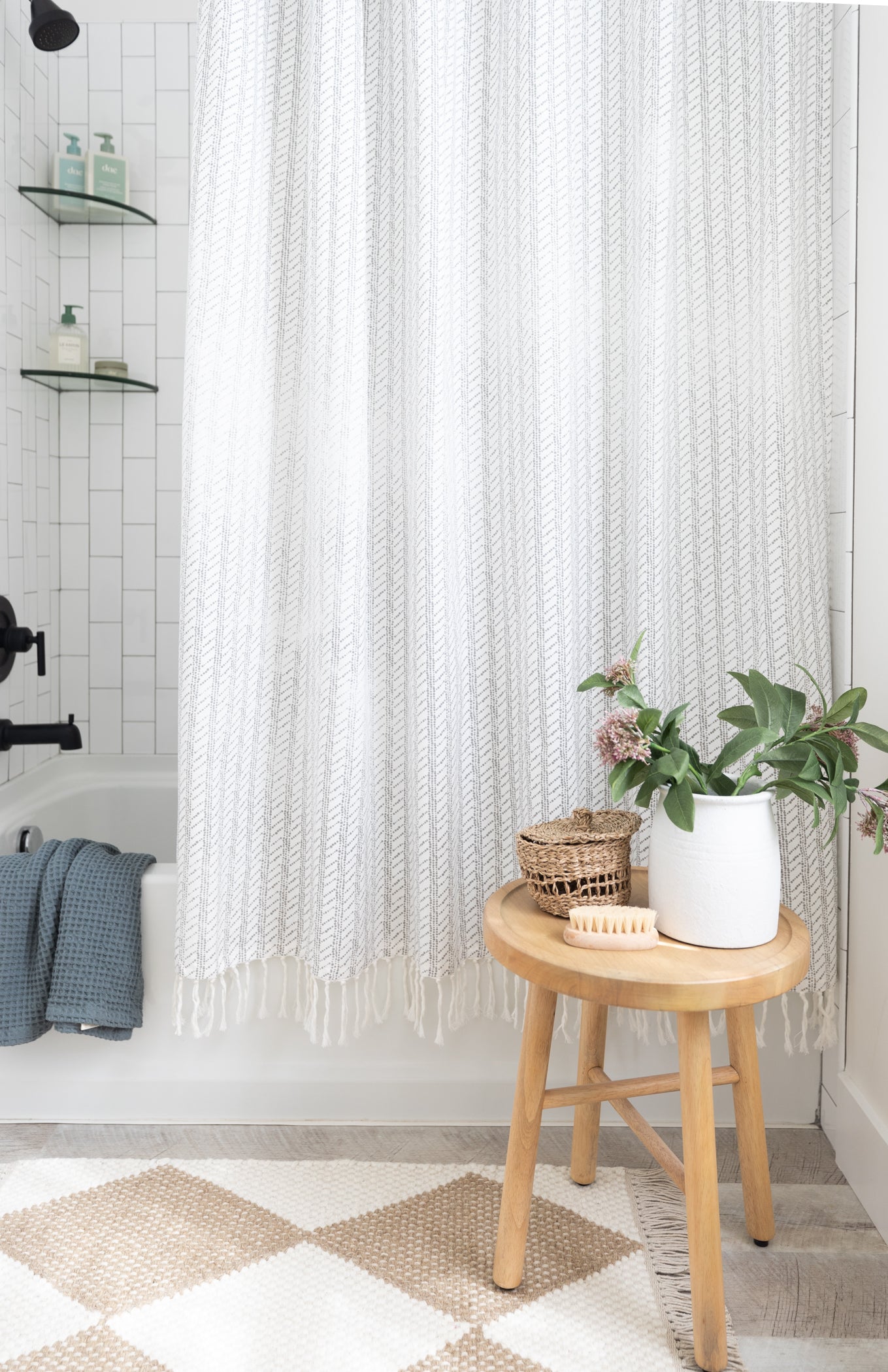 White textured shower curtain with vertical striped pattern and fringe trim hanging in bathroom.