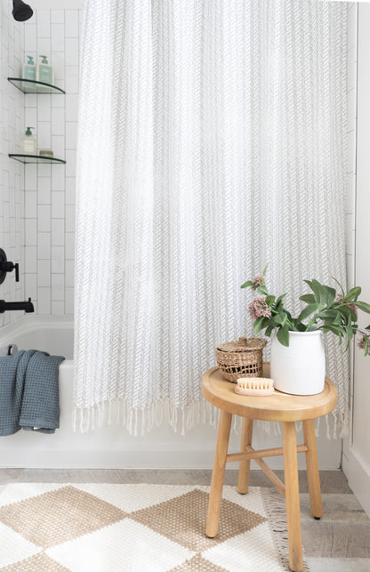 White textured shower curtain with vertical striped pattern and fringe trim hanging in bathroom.