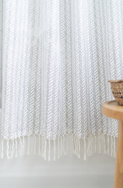 White shower curtain with gray diagonal stripe pattern and fringe trim at bottom edge.