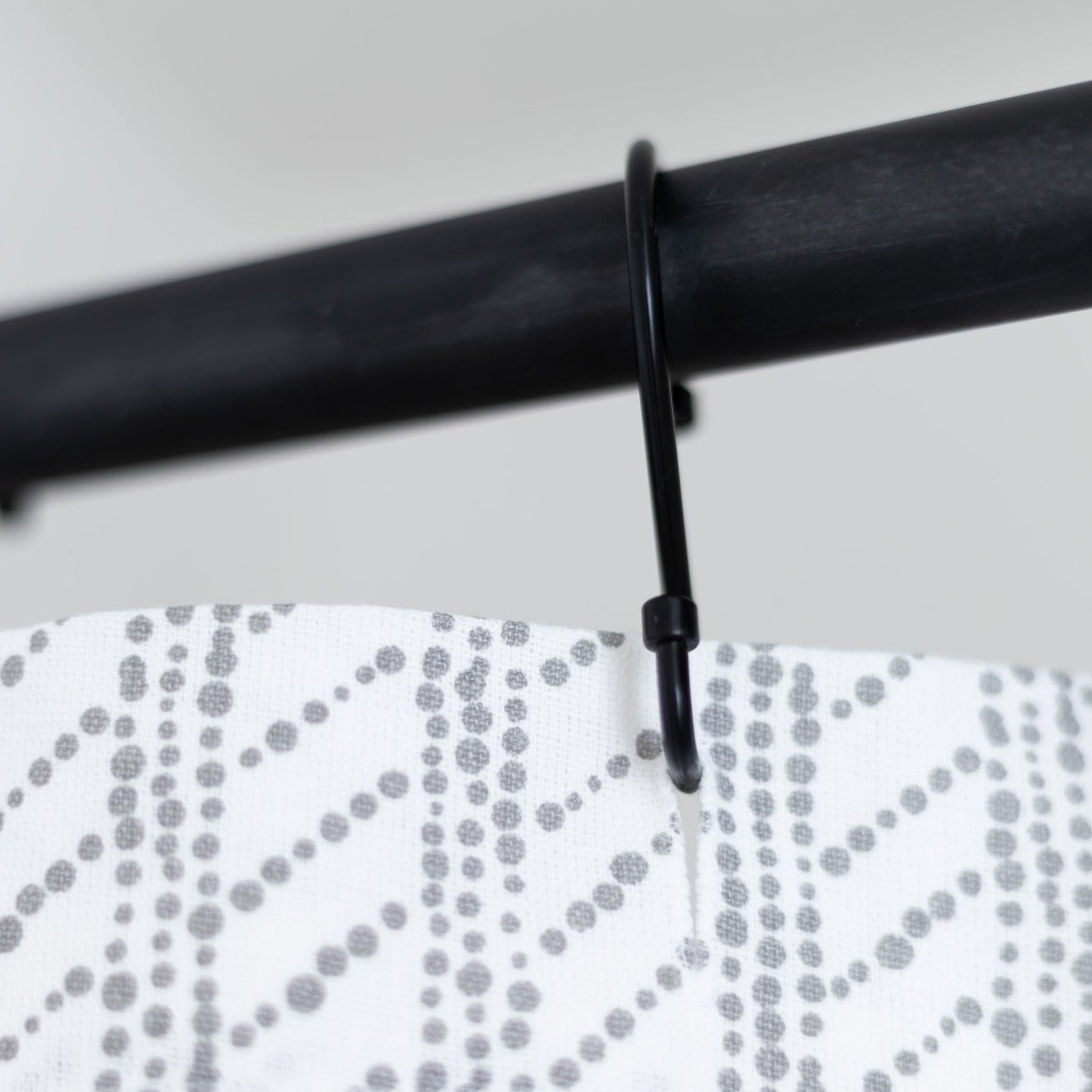 White shower curtain with gray dotted wave pattern hanging from black rod with plastic hook.