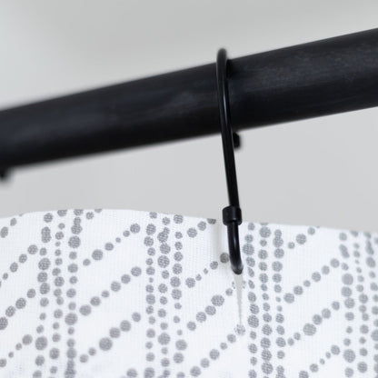 White shower curtain with gray dotted wave pattern hanging from black rod with plastic hook.