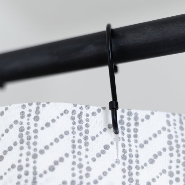 White shower curtain with gray dotted wave pattern hanging from black rod with plastic hook.