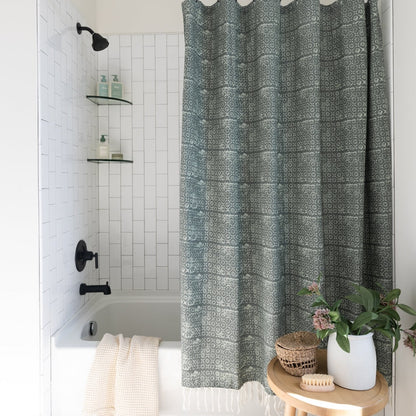 Green and white geometric patterned shower curtain hanging in a white tile bathroom with black fixtures.